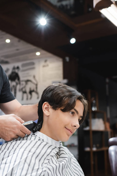 peluquero recortando el pelo de adolescente sonriente en la peluquería - Foto, imagen
