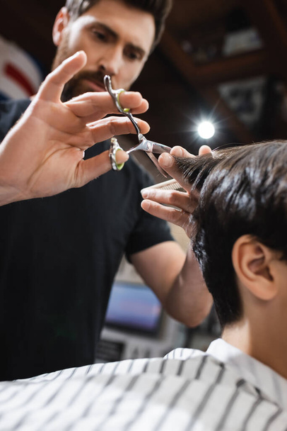 low angle view of blurred hairdresser cutting hair of teenage client in barbershop - Photo, Image