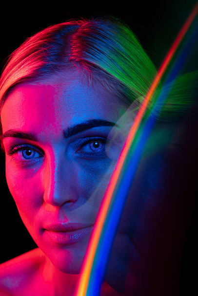 Fashion, style. Young beautiful woman with well-kept skin and stylish makeup isolated over dark background in pink neon light. Concept of natural beauty, art, emotions, cosmetics and youth - Fotoğraf, Görsel