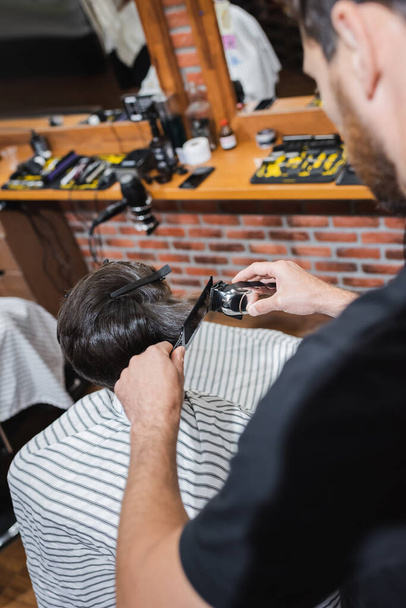 Verschwommener Friseur schneidet Haare eines Teenagers mit Klipper im Schönheitssalon  - Foto, Bild