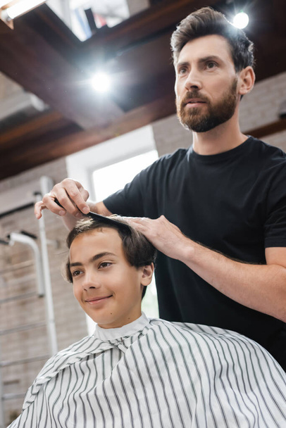 Hairdresser combing hair of teen client in beauty salon  - Фото, зображення