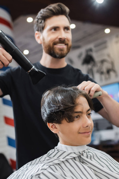 El peinado borroso el secamiento de los cabellos del muchacho adolescente en la capa en el salón de belleza  - Foto, imagen