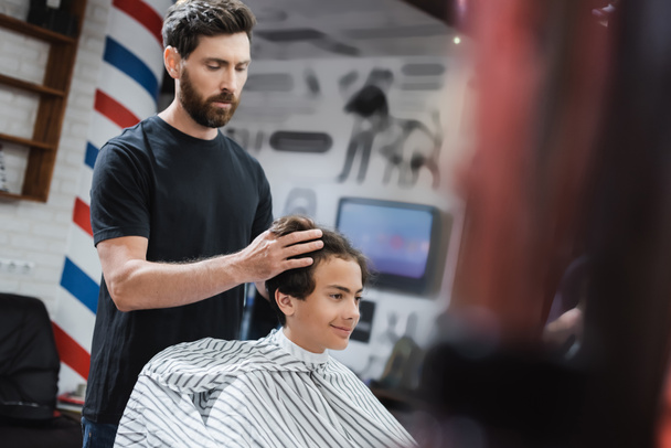 Bartfriseur stylt Haare eines lächelnden Teenagers im Schönheitssalon  - Foto, Bild