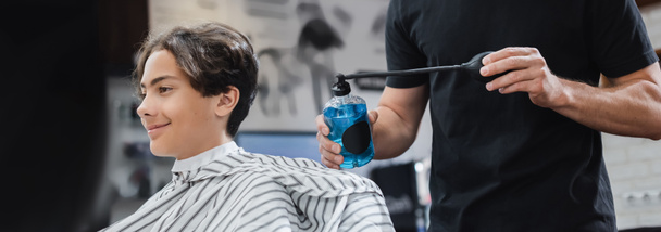 Hairstylist holding hairspray near smiling teenage boy in beauty salon, banner  - Photo, Image