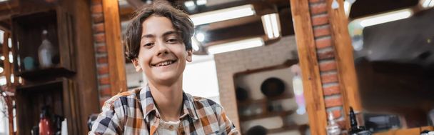 Happy teenage boy looking at camera in blurred barbershop, banner  - Fotó, kép