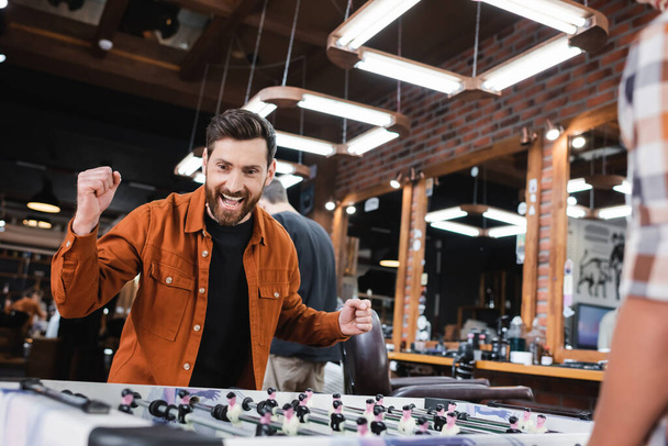 Excited man looking at table football near blurred son in barbershop  - Foto, imagen