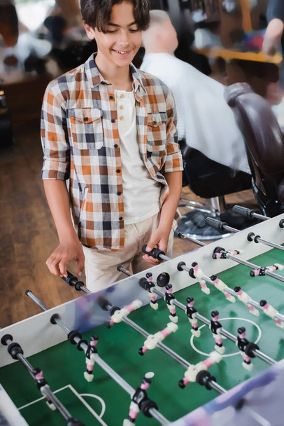 Smiling teenage boy playing table football in barbershop  - Φωτογραφία, εικόνα