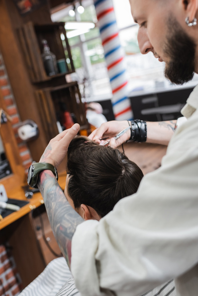 Parturi koskettaa asiakkaan hiuksia parturissa leikkauksen aikana  - Valokuva, kuva