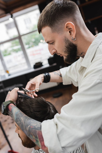 Oldalnézet tetovált borbély vágás haj az ügyfél a fodrászatban  - Fotó, kép