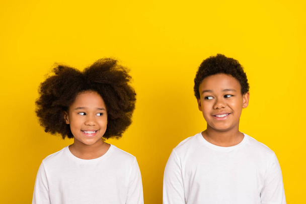 Portrait of positive minded siblings look interested each other isolated on yellow color background. - Foto, Imagen