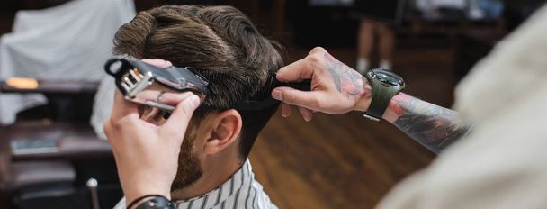 Татуйований перукар розчісує і обрізає волосся людини в перукарні, банер
  - Фото, зображення