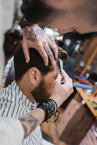 Peluquero tatuado recortar el cabello del cliente con navaja de afeitar en la barbería  - Foto, imagen
