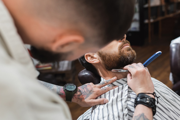 blurred hairdresser shaving neck of client with straight razor in barbershop - Zdjęcie, obraz