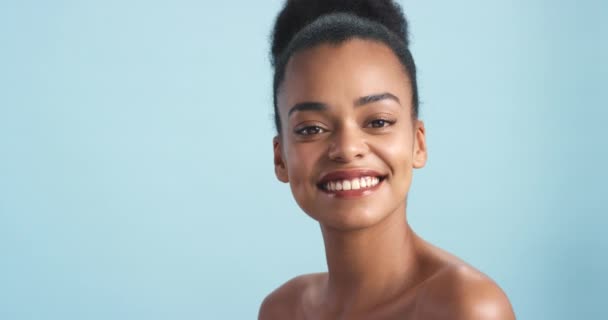 Vrolijke zwarte vrouw, glimlach en schoonheid in huidverzorging, gezondheid en welzijn tegen een blauwe studio achtergrond. Portret van een Afrikaans vrouwelijk gezicht glimlachend met tanden in geluk voor cosmetische spa behandeling. - Video