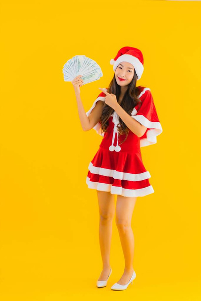 Retrato hermosa joven asiática mujer usar navidad ropa y sombrero con dinero en efectivo y dinero en amarillo aislado fondo
 - Foto, Imagen