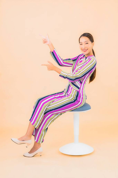 Retrato bonito jovem asiático mulher sentar na cadeira e sorrir com ação na cor isolado fundo - Foto, Imagem
