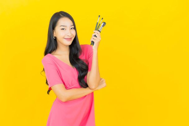 Портрет красивая молодая азиатская женщина улыбка с косметическим макияжем кисть на желтом фоне цвета - Фото, изображение