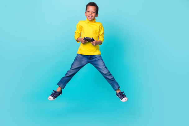 Retrato de longitud completa de niño sin preocupaciones excitado brazos de salto mantenga controlador aislado sobre fondo de color verde azulado. - Foto, imagen