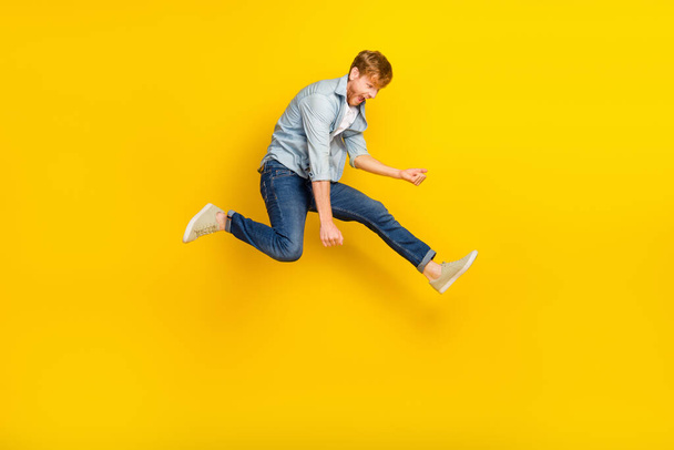Full size photo of handsome guy ginger hairdo blue shirt jeans sneakers jump play imaginary guitar isolated on yellow color background. - Foto, Imagem