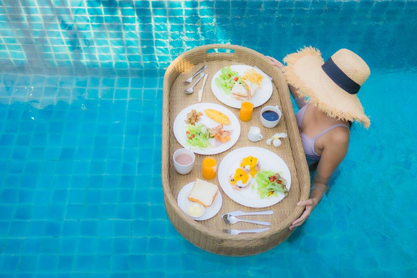 Portret młoda azjatycka kobieta szczęśliwy uśmiech cieszyć się pływające śniadanie taca w basenie w ośrodku hotelowym - Zdjęcie, obraz