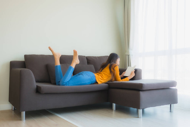 Портрет молодой азиатской женщины читать книгу на диване кресло с подушкой в интерьере гостиной - Фото, изображение