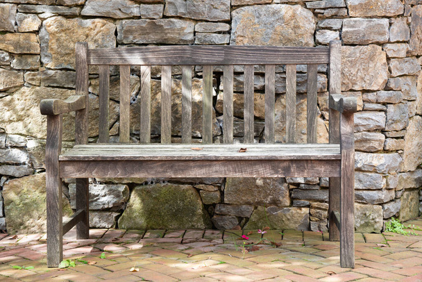 Empty, wooden park bench against a rock wall. - Photo, Image