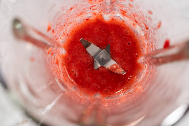 Blending fresh strawberries in a kitchen blender to prepare the strawberry buttercream frosting. - Photo, Image