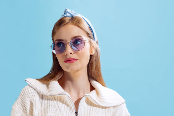 Portrait of young beautiful woman posing in stylish sunglasses isolated over blue studio background. Youth fashion. Concept of beauty, lifestyle, youth, emotions, facial expression, ad. - Valokuva, kuva