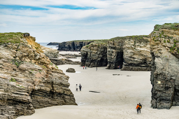 People walking on Cathedrals Beach at low tide, Playa las Catedrales in Ribadeo, province of Lugo, Galicia. Cantabric coast in northern Spain. Tourist place. - Фото, изображение