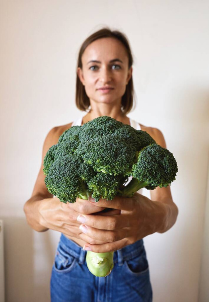 young woman dressed in white t-shirt showing with broccoli. High quality photo - Fotografie, Obrázek