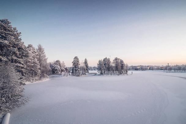 Frosty ochtend in de Finse stad Kajaani in het noorden van het land in de regio Kainu. Uitzicht op de bevroren Kajaaninjoki rivier en het besneeuwde bos bij de rivier. Zonsopgang. - Foto, afbeelding