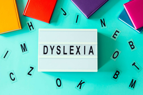 Dyslexia awareness, help children with reading, learning difficulties concept. Lightbox with DYSLEXIA word. Colorful books and different letters on light blue background. Top view. - Photo, Image