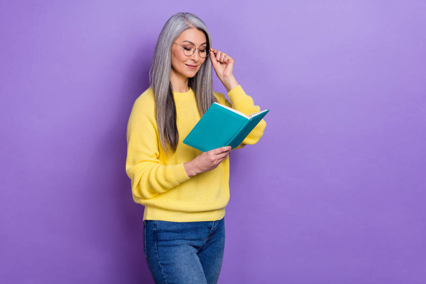 Photo of clever pretty lady pensioner dressed pullover arms eyewear reading fiction literature isolated purple color background. - Foto, immagini