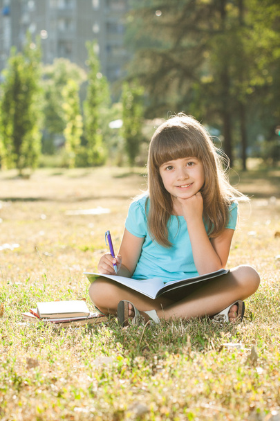 Little schoolgirl doing her homework in the park - 写真・画像