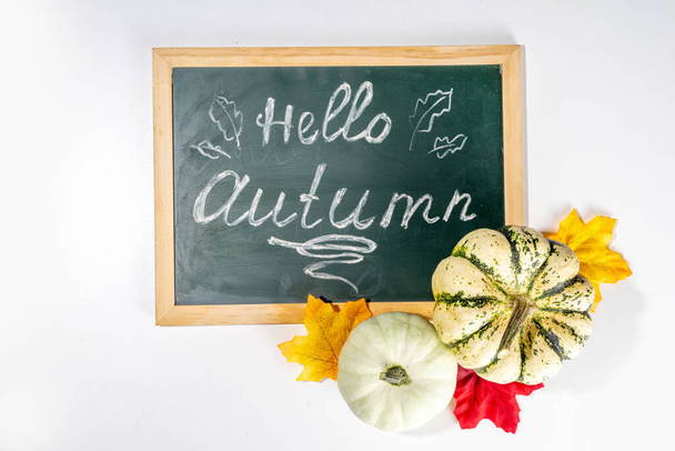 Őszi dekoratív sütőtök őszi levelek fehér asztal háttér. Őszi Hálaadás halloween ünnep üdvözlőlap háttér, betakarítás koncepció. Felülnézet, másolás - Fotó, kép