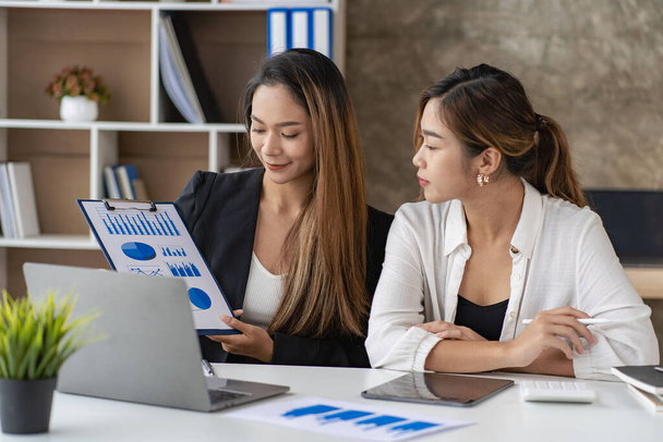 Un equipo de empresarias asiáticas discutiendo algo y sonriendo mientras se sientan en un escritorio en la oficina de mujeres que trabajan juntas analizando las finanzas. - Foto, imagen