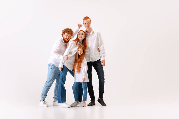 Happy family, red-haired young men, woman and kid wearing casual style clothes spend time together at studio photo shoot. Look delighted, thrilled. Concept of emotions, love, fashion, relationship - Foto, Imagen