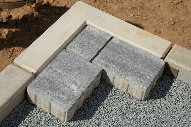 Het leggen van grijze betonnen plavuizen op de binnenplaats van het huis op een zandfundering. - Foto, afbeelding