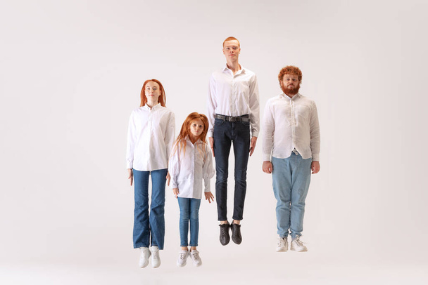 Levitation and calmness. Two men and woman and kid, red-headed young people wearing casual style clothes flighting over white background. Creativity, inspiration, art, fashion, emotions, style. - Фото, изображение