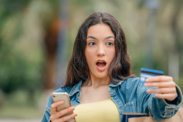meisje met mobiele telefoon en creditcard met een verrast of verbaasd uitdrukking - Foto, afbeelding