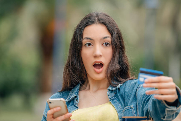 fille avec téléphone portable et carte de crédit avec une expression surprise ou étonnée - Photo, image
