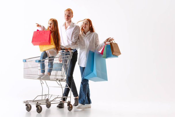 Wow. Happy and excited family, young readhaired people walking together after shopping with purchases in hands isolated on white bakground. Concept of black Friday, holidays, fashion, dreams - Foto, Imagen
