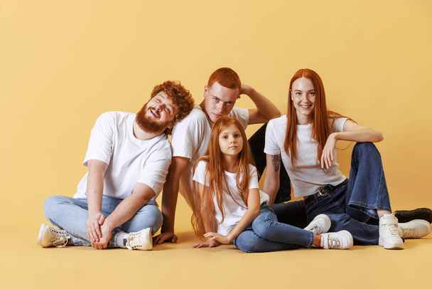 Friendly family, redhead young men, woman and kid wearing casual style clothes spend time together at studio photo shoot. Look delighted, thrilled. Concept of emotions, love, fashion, relationship - Photo, Image
