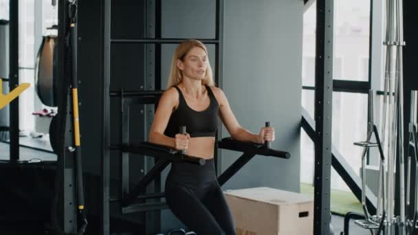 Abs workout. Sporty middle aged woman athlete exercising on sport bars at gym, lifting her legs, practicing body strength training, slow motion, free space - Footage, Video