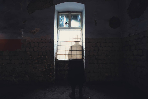 A mysterious figure wearing a long coat and fedora standing in a ruined, abandoned house - Foto, afbeelding