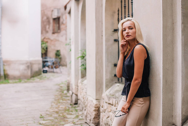 A young, blonde girl in a black blouse and sunglasses poses against the backdrop of an old courtyard in Lviv. Ukraine. High quality photo - Foto, Bild
