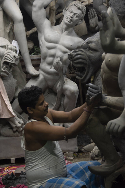 Een man schildert Durga idool met selectieve focus op een bepaald deel van de man met de rest van de man, het idool en al het andere wazig. Kolkata, West-Bengalen, India - 11.09.2022 - Foto, afbeelding