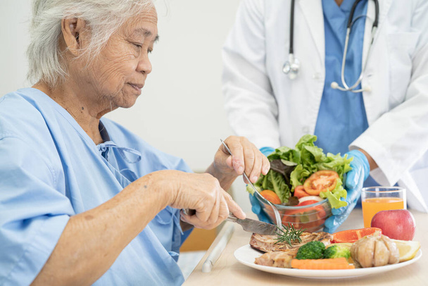 Asiatico anziano o anziano donna anziana paziente mangiare colazione e verdura cibo sano con speranza e felice mentre seduto e affamato sul letto in ospedale. - Foto, immagini