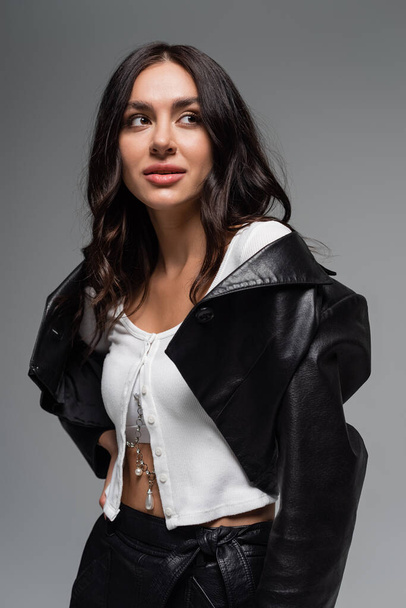 brunette young woman in black leather jacket looking away while posing isolated on grey - Zdjęcie, obraz