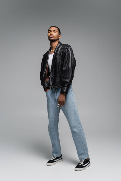 full length of young african american man in jeans and leather black jacket on grey - Фото, зображення